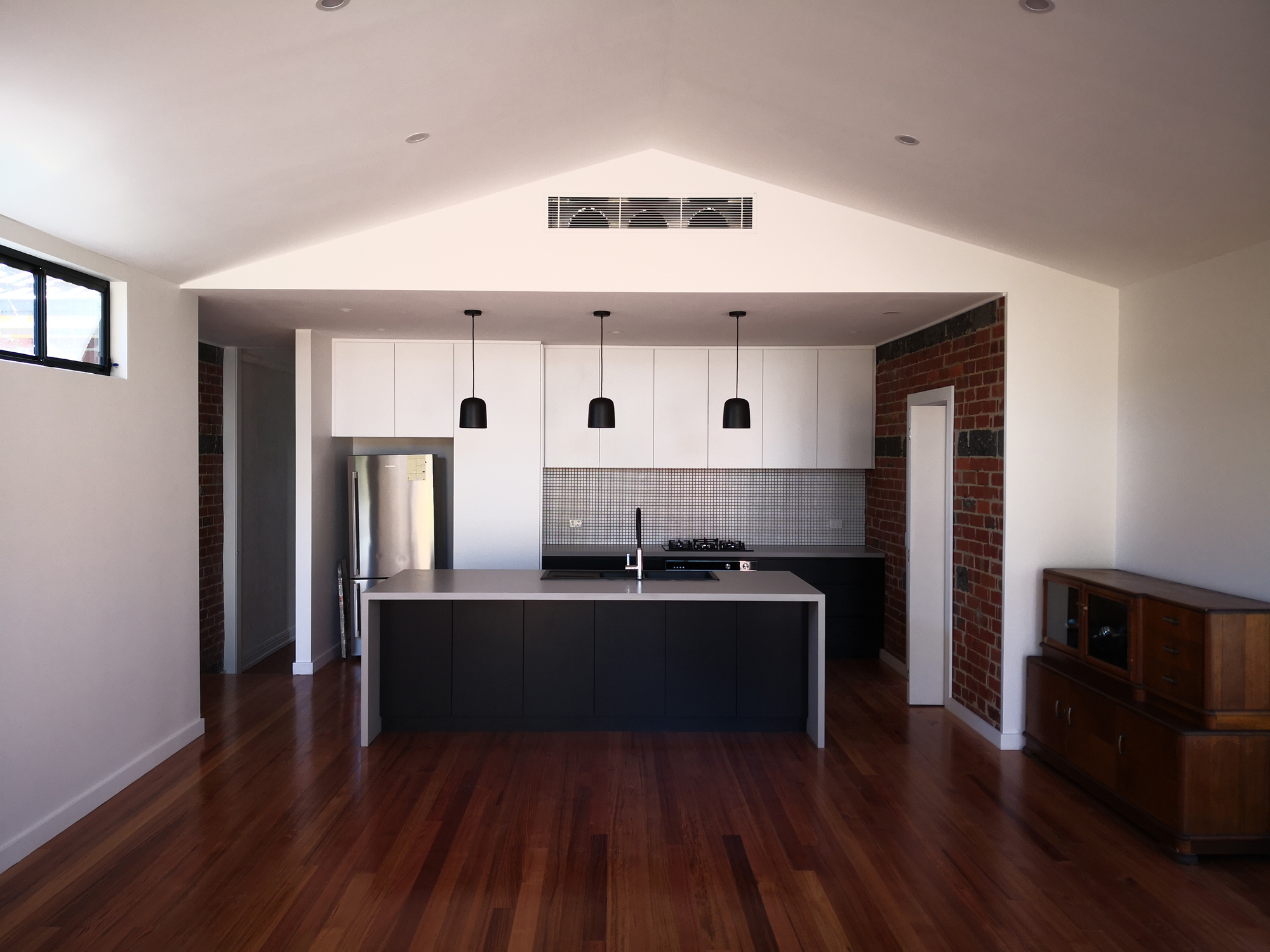 kitchen with bold, dark coloured accents, hanging pendants and an exposed brick feature wall